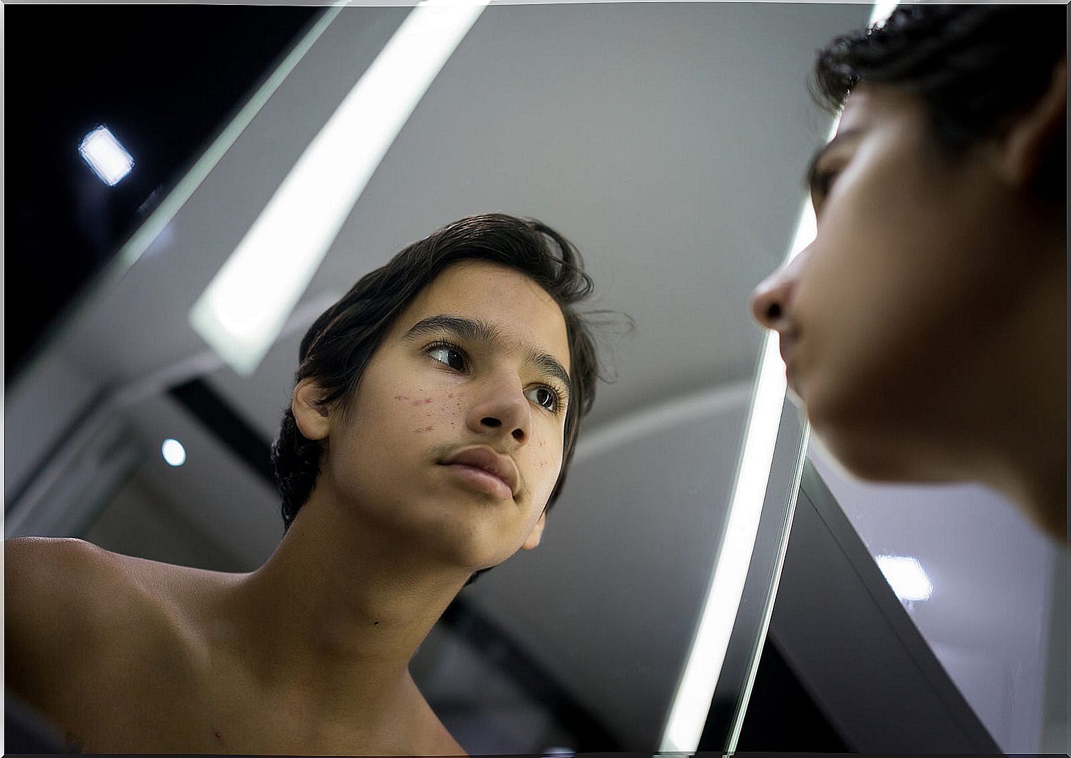 Teen boy looking in the mirror because he suffers from body dysmorphic disorder.