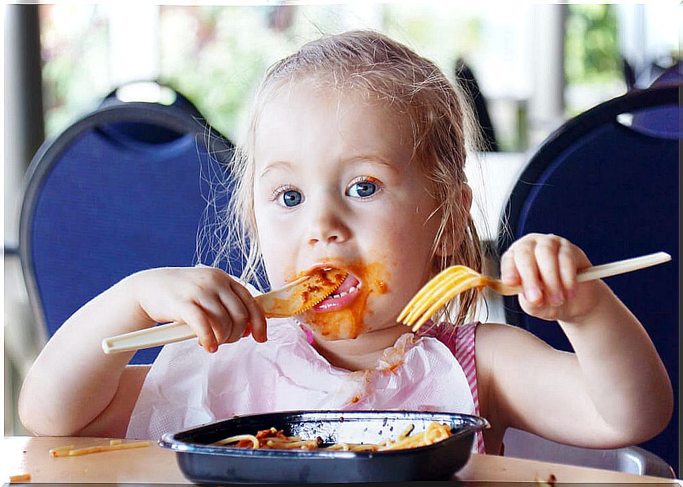 Little girl eating pasta with tomato in a restaurant.